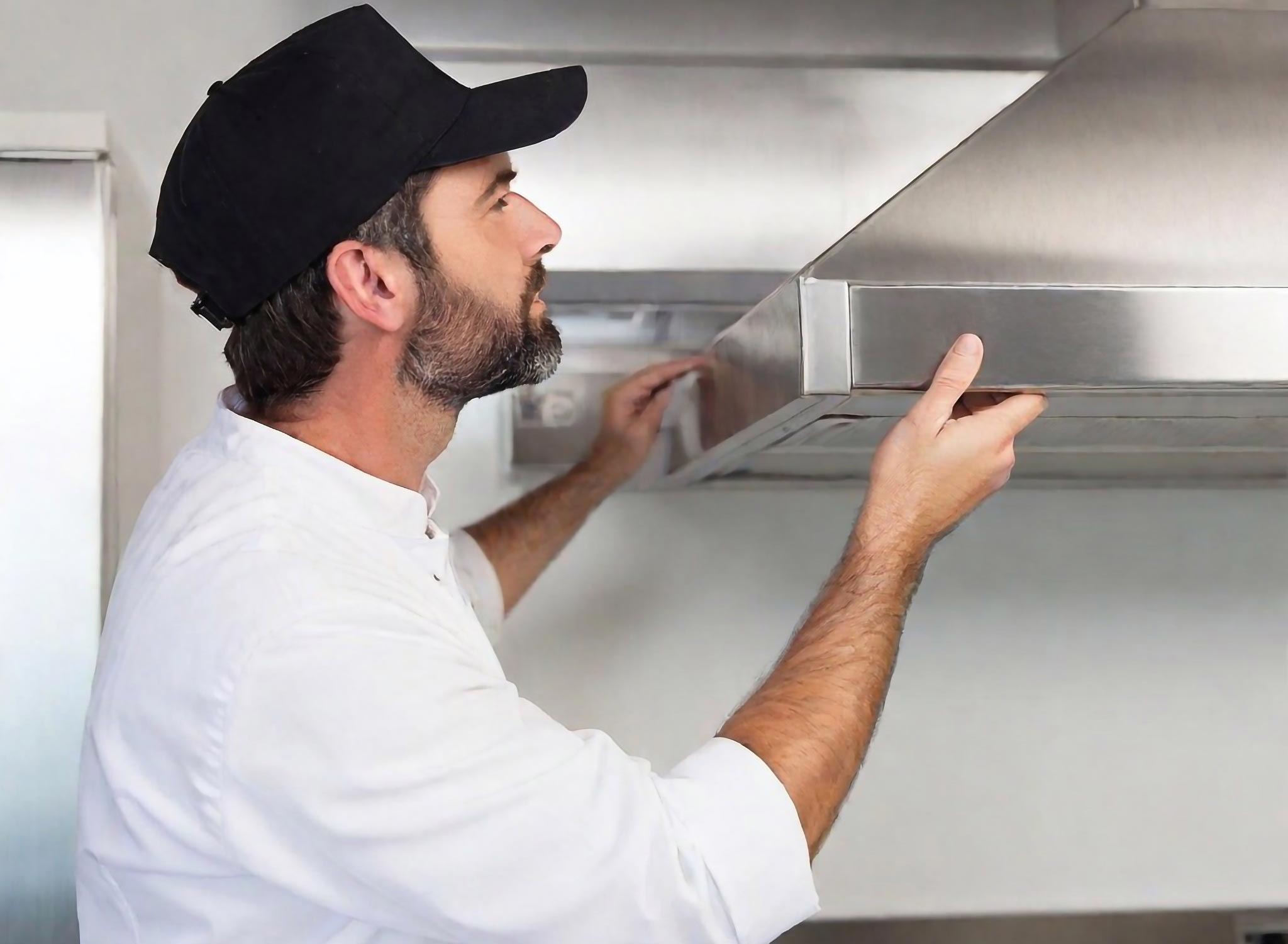 A professional cleaner working in a commercial kitchen cleaning the vent hood.